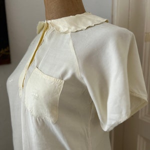 May include: A white, short-sleeved blouse with a Peter Pan collar and a single pocket on the left side.