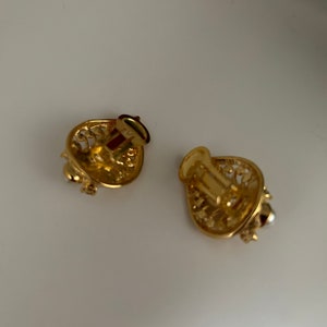 May include: A pair of gold-tone clip-on earrings with a delicate filigree design. One earring features a small pearl accent.