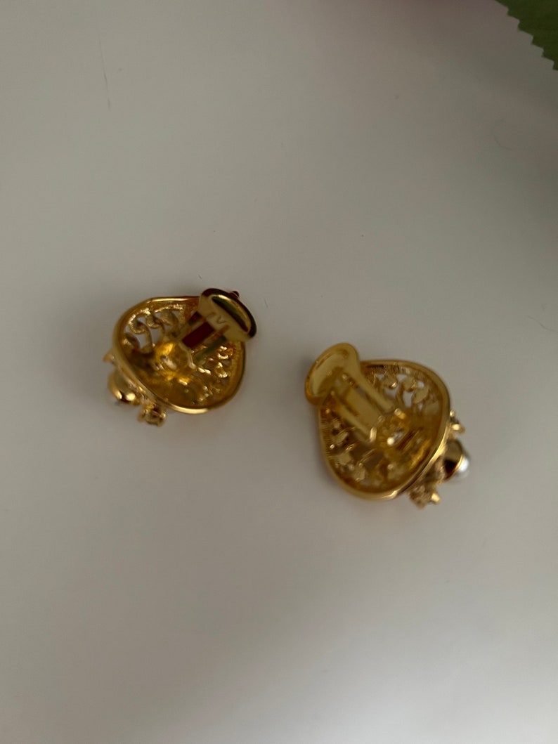 May include: A pair of gold-tone clip-on earrings with a delicate filigree design. One earring features a small pearl accent.