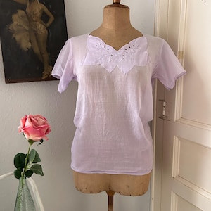May include: A light purple sheer blouse with a delicate embroidered neckline featuring a butterfly design.