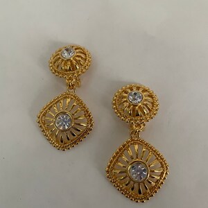 May include: A pair of gold tone clip-on earrings with a square design and clear rhinestones.