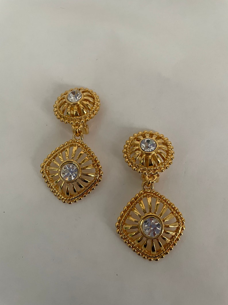 May include: A pair of gold tone clip-on earrings with a square design and clear rhinestones.