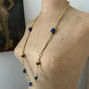 May include: A gold chain necklace with oval-shaped blue, green, and red beads. The necklace is displayed on a mannequin.