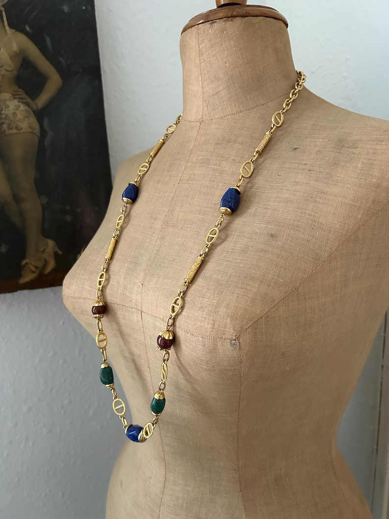 May include: A gold chain necklace with oval-shaped blue, green, and red beads. The necklace is displayed on a mannequin.