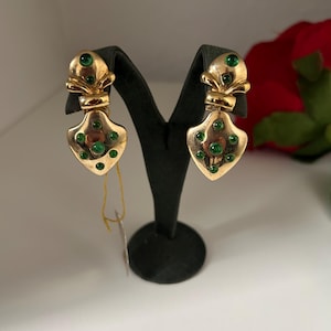 May include: A pair of gold earrings with green gemstones. The earrings are shaped like a heart with a small crown on top.
