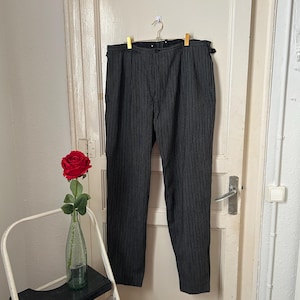 Könnte beinhalten: Schwarz-weiß gestreifte Hose, die an einem Kleiderbügel an einer weißen Tür hängt. Die Hose hat eine hohe Taille und ein gerades Bein.