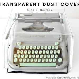 May include: A clear plastic dust cover for a vintage Hermes typewriter. The cover is labelled "Size L" and "Hermes".