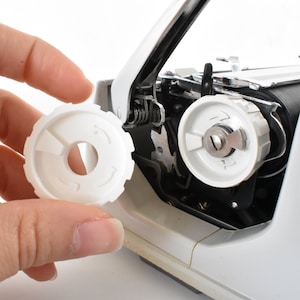 Pode incluir: Uma engrenagem de plástico branco para uma máquina de escrever. A engrenagem tem um furo no centro e uma série de dentes ao redor da borda.