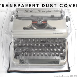 May include: A clear plastic dust cover for a vintage Olympia typewriter. The cover is designed to protect the typewriter from dust and dirt. The cover is labeled "Size L, Olympia".
