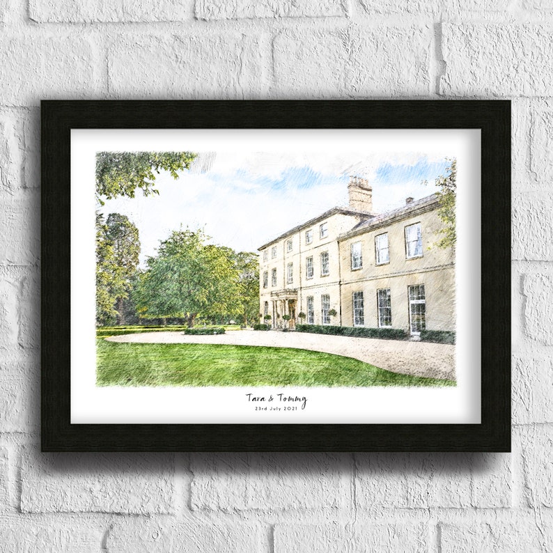 May include: A framed print featuring a pencil sketch of a large, light-colored building with multiple windows, set against a backdrop of green trees and a blue sky. The print is in a black frame, with the names "Tara & Tommy" and the date "23rd July 2021" at the bottom.