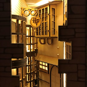 May include: A wooden model of a Harry Potter themed alleyway with a sign that reads "Leaky Cauldron" and a sign that reads "HP". The alleyway is lit with warm yellow lights and has a brick wall on the right side.