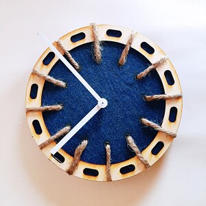 May include: A wooden clock with a blue denim face and white hands. The clock has a decorative rope design around the edge.