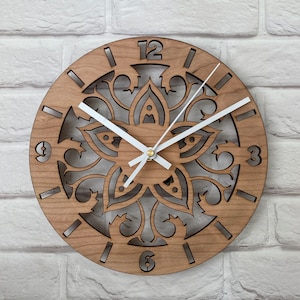 May include: A wooden wall clock with a decorative, laser-cut design featuring a floral pattern. The clock face has white hands and black Roman numeral markings.