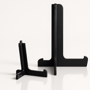 Puede incluir: Dos soportes de exhibición de madera negra. Uno es pequeño e inclinado, el otro es más grande y vertical. Ambos tienen un diseño simple y minimalista, ideal para exhibir artículos. Hecho de madera.