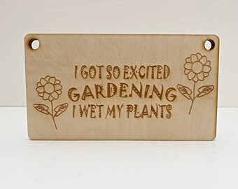 Może przedstawiać: Prostokątny drewniany znak z wygrawerowanym tekstem "I GOT SO EXCITED GARDENING I WET MY PLANTS". Znak ma dwa otwory u góry i ilustracje kwiatów. Drewno ma jasnobrązowy kolor.