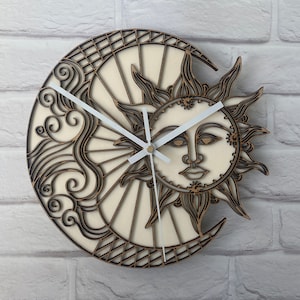 May include: Wooden wall clock with a sun and moon design. The clock has a layered design with a light beige background and brown accents. The sun has a face, and the moon is crescent-shaped. White clock hands show the time.