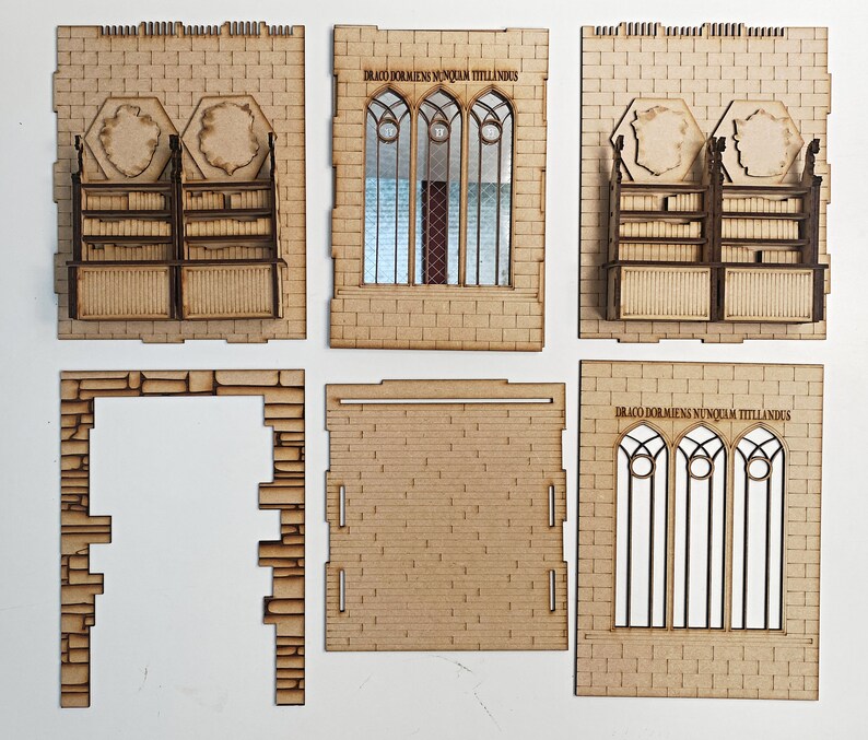 Op de afbeelding: Een set van zes lasergesneden houten stukken voor het bouwen van een model van een middeleeuws gebouw. De stukken omvatten een raam met de Latijnse tekst "Draco Dormiens Nunquam Titillandus", een boekenkast en een bakstenen muur.