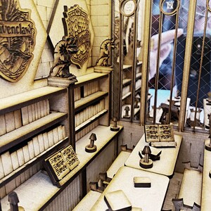 Op de afbeelding: Een houten model van een bibliotheek van Zweinstein met vier huiswapens, boekenkasten, bureaus en lampen. De wapens zijn voor Griffoendor, Huffelpuf, Zwadderich en Ravenklauw.