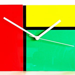 May include: A colourful clock with a red, yellow, green and black design. The clock hands are white.