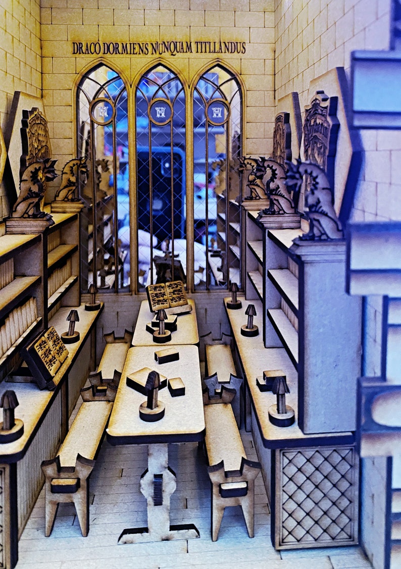 Op de afbeelding: Een houten model van een kamer met een groot raam, boekenkasten en een tafel met stoelen. De kamer is versierd met drakenbeelden en de tekst "DRACO DORMIENS NUNQUAM TITTILANDUS" staat boven het raam.