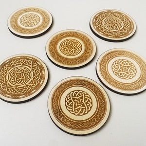 May include: Six round wooden coasters with a Celtic knot design in brown and beige. The coasters are made of natural wood and have a smooth finish.