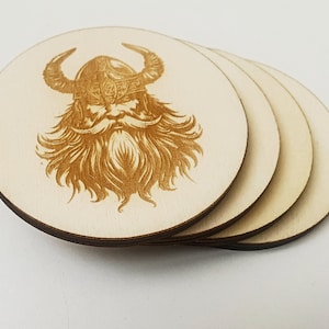 Op de afbeelding: Een set van vier ronde onderzetters van lichtgekleurd hout, licht versprongen gestapeld. Elke onderzetter is voorzien van een donkerbruine, met laser gegraveerde afbeelding van een Vikingkrijger met een gehoornde helm en baard.