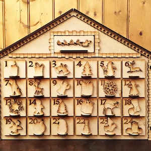 Könnte beinhalten: Weihnachts-Adventskalender aus Holz in Form eines Hauses. Der Kalender hat 24 nummerierte Türen, jede mit einem festlichen Ausschnitt. Ein Weihnachtsmann und Rentierschlitten befinden sich über den Türen. Der Kalender ist aus hellem Holz gefertigt.