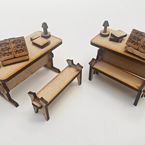 Op de afbeelding: Twee miniatuurhouten bureaus met banken, elk met een boek en een lamp. De bureaus zijn gemaakt van lichtbruin hout en de banken van donkerbruin hout.