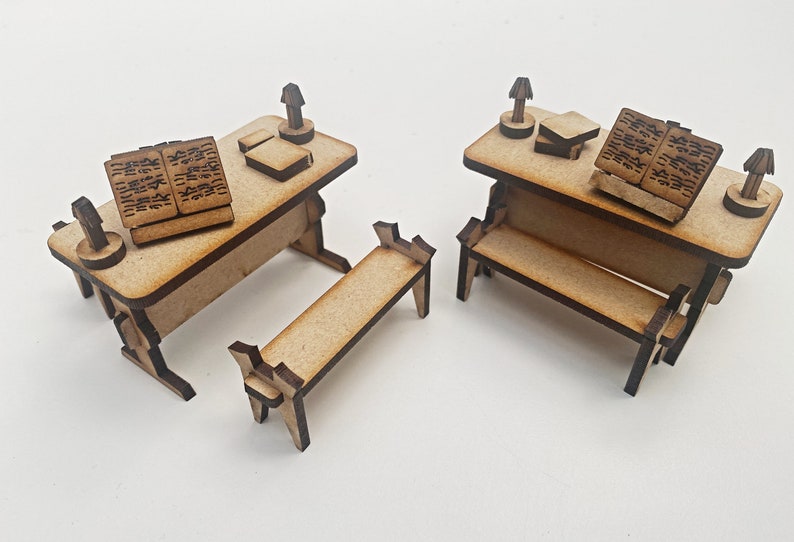 Op de afbeelding: Twee miniatuurhouten bureaus met banken, elk met een boek en een lamp. De bureaus zijn gemaakt van lichtbruin hout en de banken van donkerbruin hout.