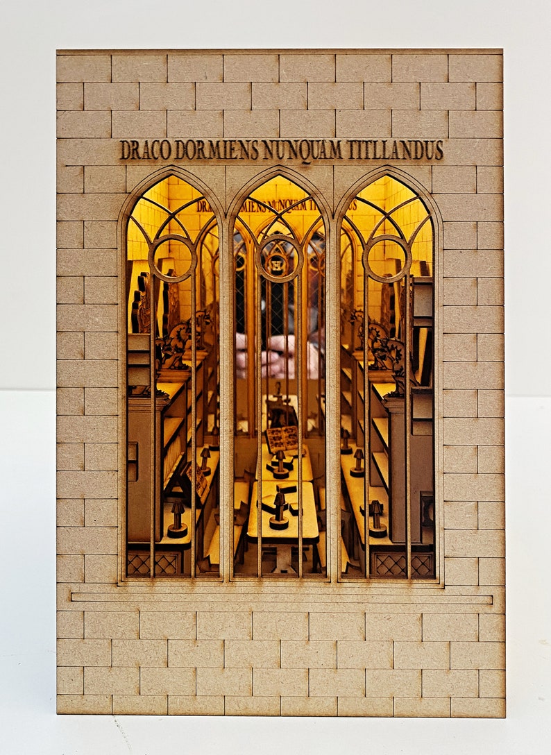 Op de afbeelding: Een houten model van een bakstenen gebouw met drie boogvensters. De ramen zijn van hout en hebben een rasterpatroon. De tekst "DRACO DORMIENS NUNQUAM TITTILLANDUS" staat boven de ramen.