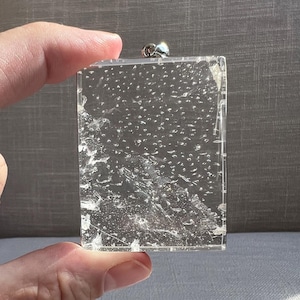 May include: A clear glass pendant with a silver metal loop. The glass has a textured surface with small bubbles throughout.