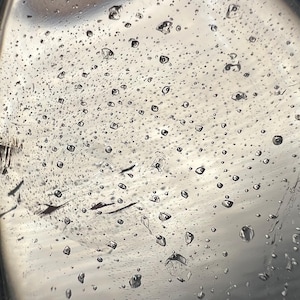 May include: A close-up of a silver surface covered in water droplets. The droplets are round and clear, and they reflect the light.