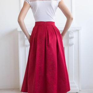 Stylish midi red skirt with a wide pleats. Waist fit, has a sewn-in waistband about two inches wide. Made of polished cotton, with a slight sheen. Pockets in the side seams. Wide cuff at the bottom to keep skirt's shape. Hidden zip at the back.