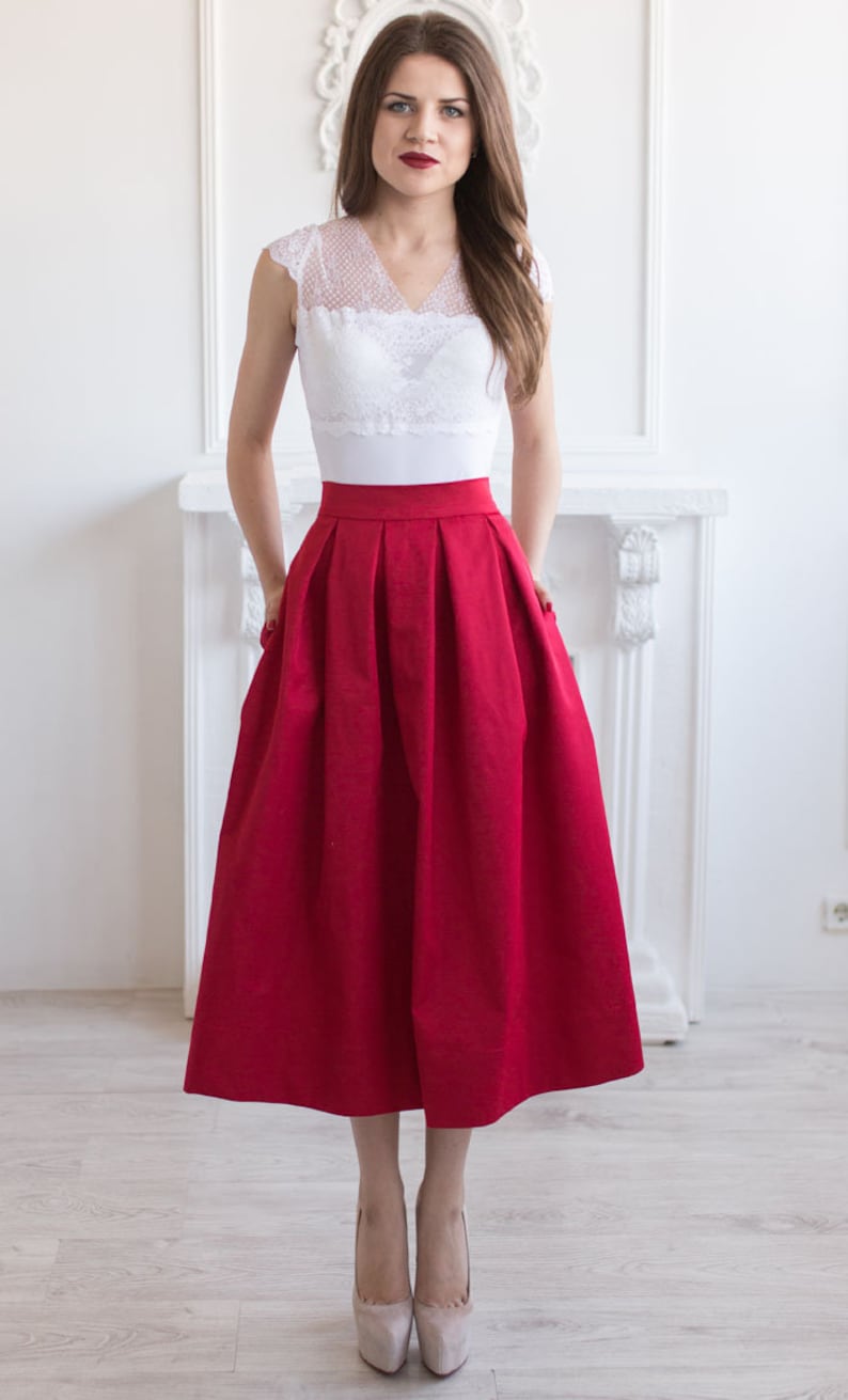 Stylish midi red skirt with a wide pleats. Waist fit, has a sewn-in waistband about two inches wide. Made of polished cotton, with a slight sheen. Pockets in the side seams. Wide cuff at the bottom to keep skirt's shape. Hidden zip at the back.