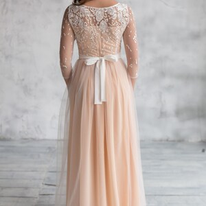 May include: A long, peach-coloured tulle dress with a white lace bodice and a white satin sash tied at the waist.