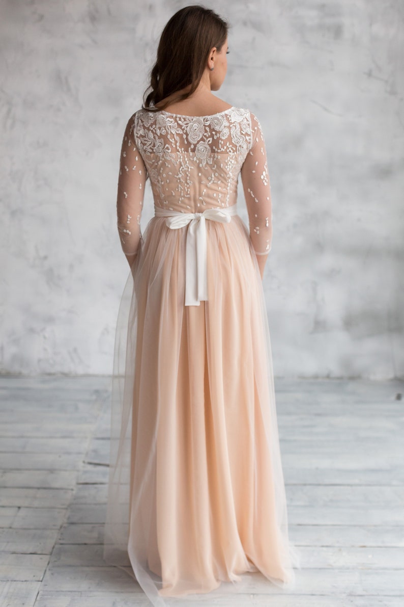 May include: A long, peach-coloured tulle dress with a white lace bodice and a white satin sash tied at the waist.