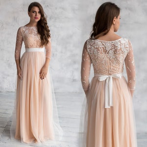 May include: A long, peach-coloured tulle dress with a white lace bodice and a white satin sash. The dress has a scoop neckline and three-quarter sleeves.