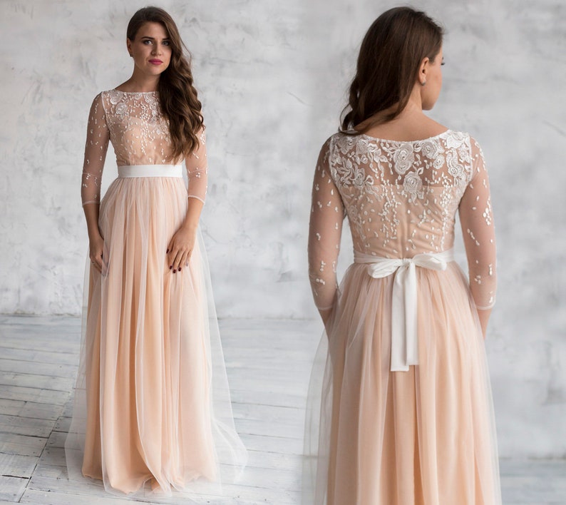 May include: A long, peach-coloured tulle dress with a white lace bodice and a white satin sash. The dress has a scoop neckline and three-quarter sleeves.