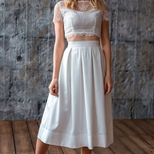 Stylish midi ivory skirt with a wide pleats. Waist fit, has a sewn-in waistband about two inches wide. Made of polished cotton, with a slight sheen. Pockets in the side seams. Wide cuff at the bottom to keep skirt's shape. Hidden zip at the back.