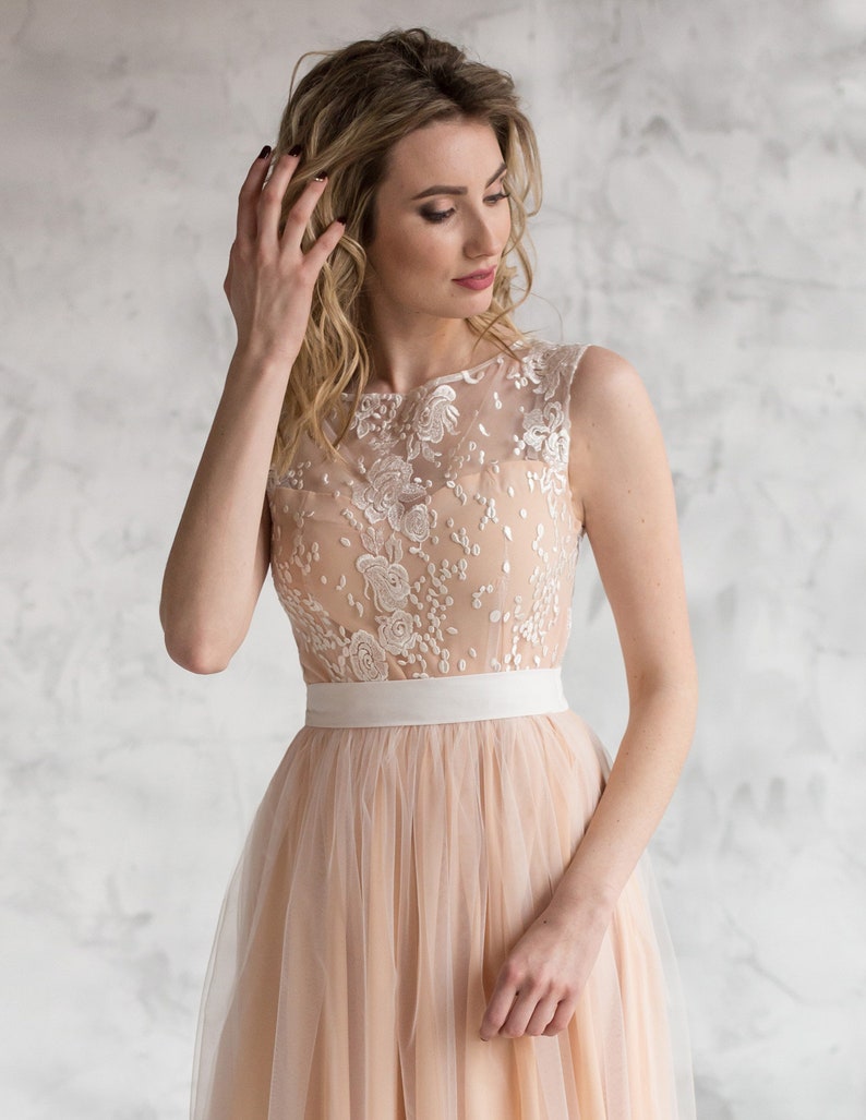 Puede incluir: Un vestido de tul rosa claro con un corpi&ntilde;o de encaje blanco y una faja de sat&eacute;n blanco. El vestido es sin mangas y tiene una falda fluida.