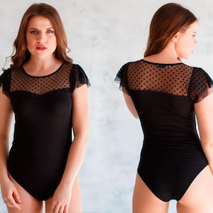 May include: Black bodysuit with a sheer polka dot mesh panel at the neckline and short sleeves. The bodysuit has a lace trim around the neckline.