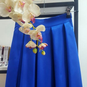 Stylish midi blue skirt with a wide pleats. Waist fit, has a sewn-in waistband about two inches wide. Made of polished cotton, with a slight sheen. Pockets in the side seams. Wide cuff at the bottom to keep skirt's shape. Hidden zip at the back.