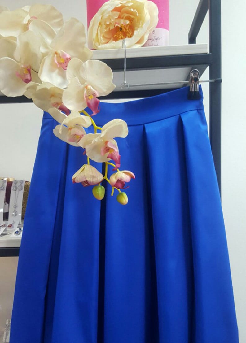 Stylish midi blue skirt with a wide pleats. Waist fit, has a sewn-in waistband about two inches wide. Made of polished cotton, with a slight sheen. Pockets in the side seams. Wide cuff at the bottom to keep skirt's shape. Hidden zip at the back.