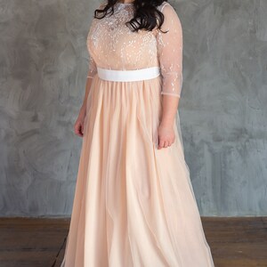 May include: A woman wearing a peach tulle gown with a white lace bodice and a white satin sash. The gown has a long skirt and is floor-length.