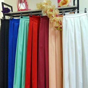 May include: A display of colorful, pleated skirts hanging on a rack. The skirts are in various colors, including black, blue, teal, red, burgundy, peach, and white. The skirts are made of a smooth, flowing fabric.