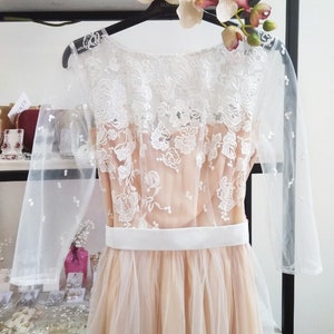 May include: A long, tulle dress with a white lace overlay and a white satin sash. The dress has a scoop neckline and three-quarter sleeves.