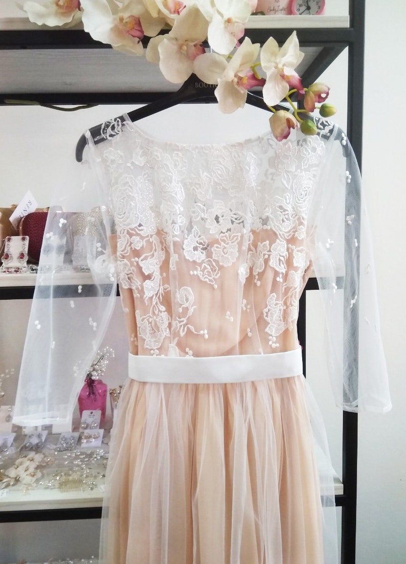 May include: A long, tulle dress with a white lace overlay and a white satin sash. The dress has a scoop neckline and three-quarter sleeves.