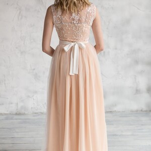 Puede incluir: Un vestido maxi de tul color melocot&oacute;n con un corpi&ntilde;o de encaje blanco y una faja de sat&eacute;n blanco atada en un lazo en la espalda.