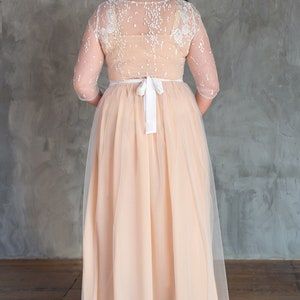 May include: A long, peach-coloured tulle dress with a white lace bodice and a white satin ribbon at the waist.