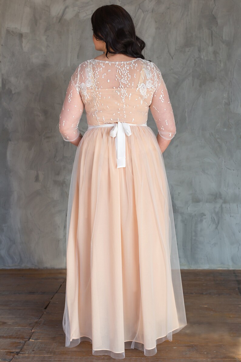 May include: A long, peach-coloured tulle dress with a white lace bodice and a white satin ribbon at the waist.